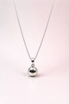 Silver necklace with a round ball pendant on a light pink background