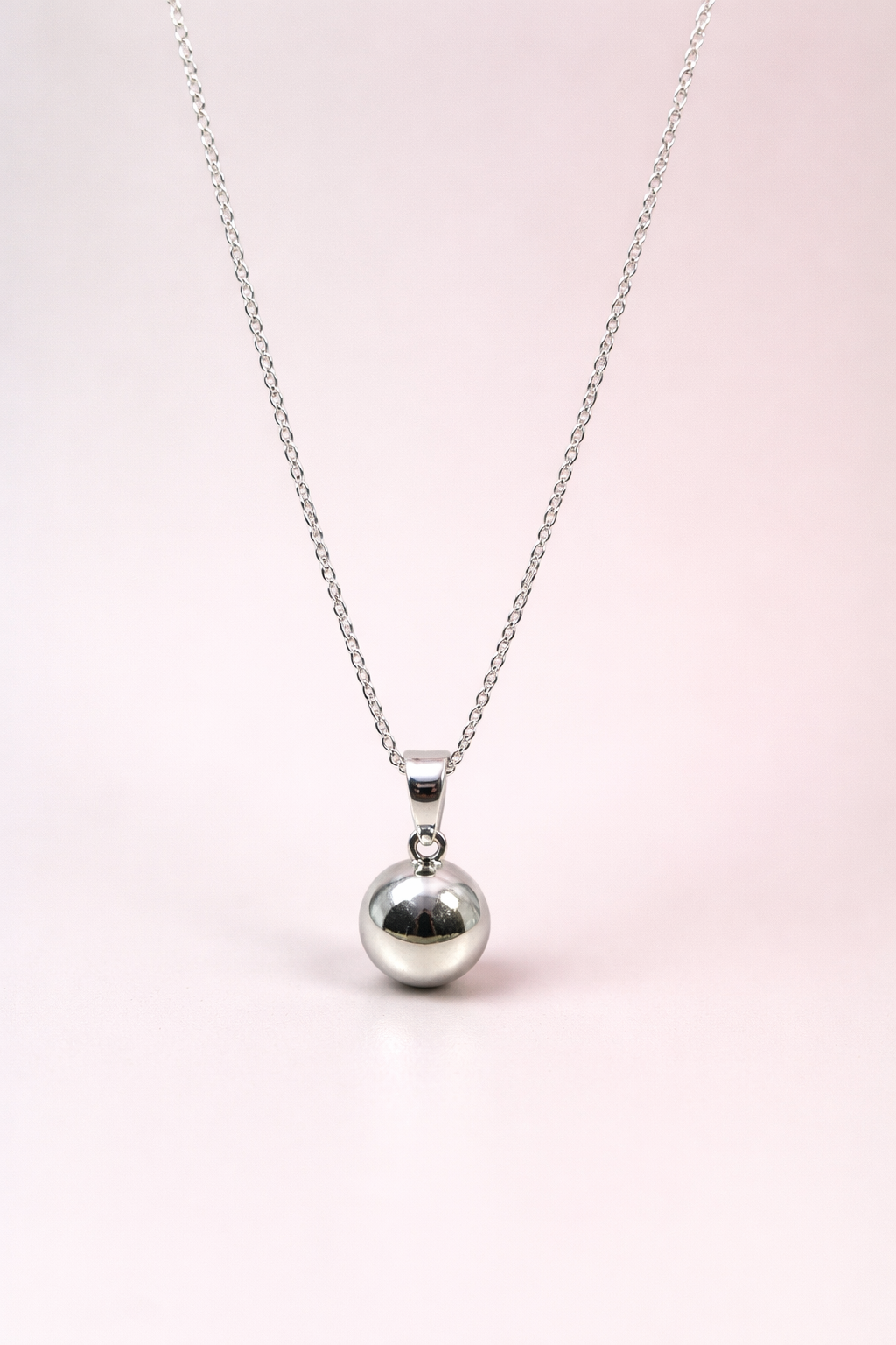 Silver necklace with a round ball pendant on a light pink background