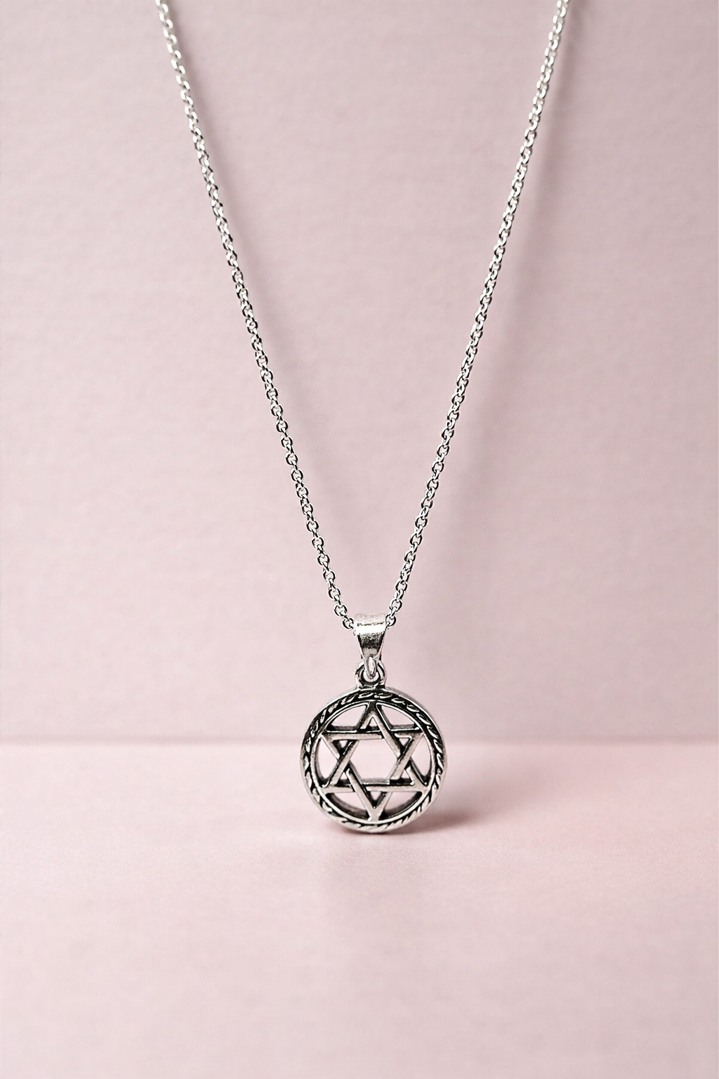 Silver necklace with a Star of David pendant on a pink background