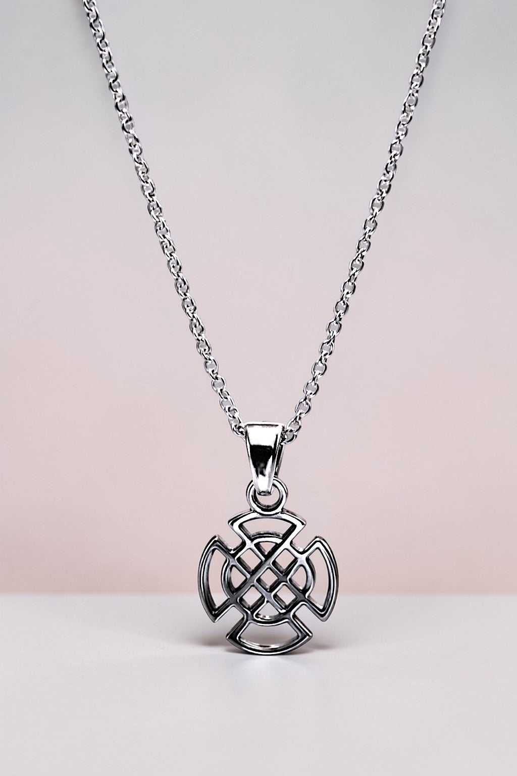 Silver necklace with a Celtic knot pendant on a light pink background