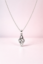 Silver Celtic knot pendant on a chain against a light pink background