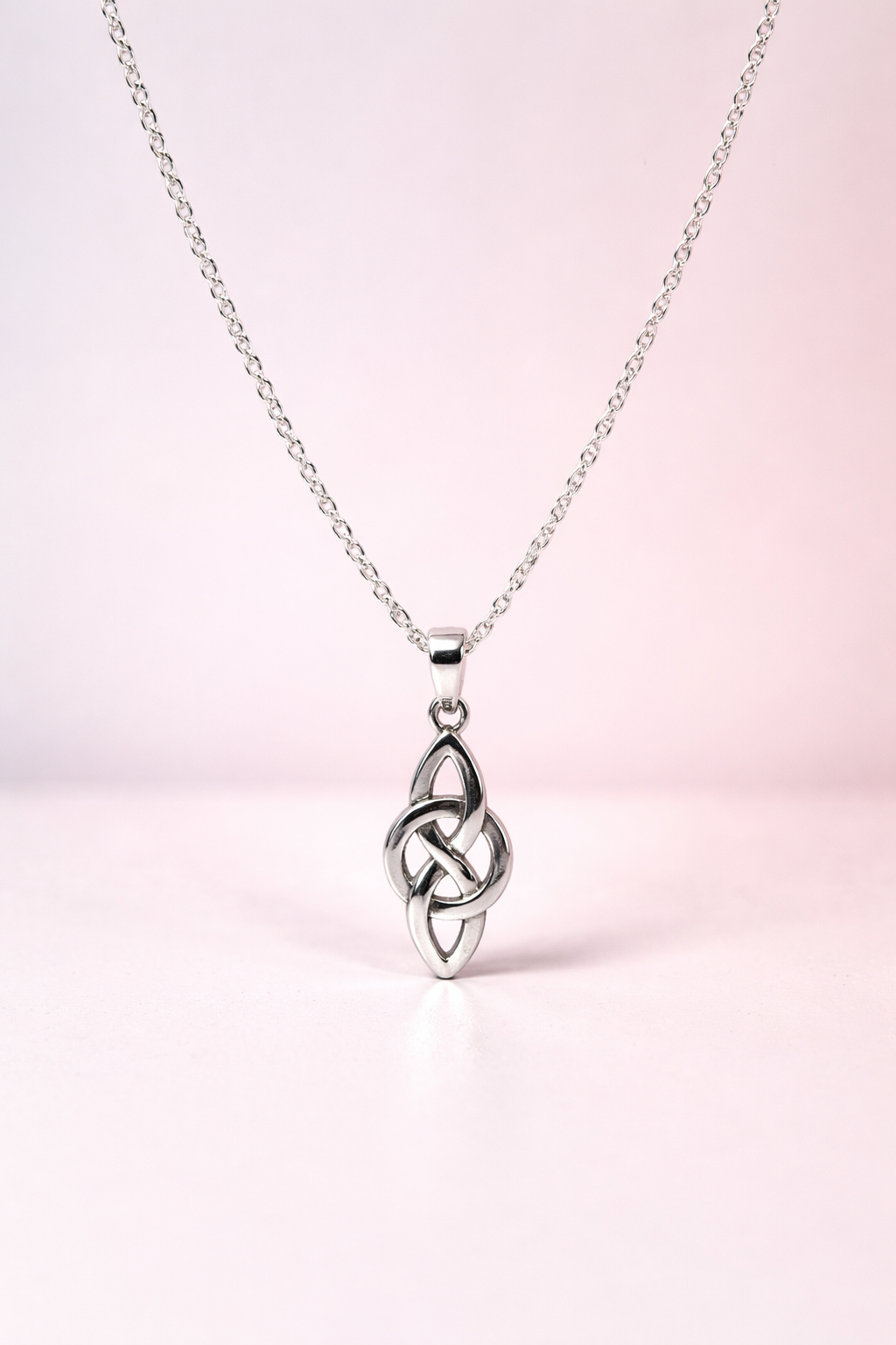 Silver Celtic knot pendant on a chain against a light pink background