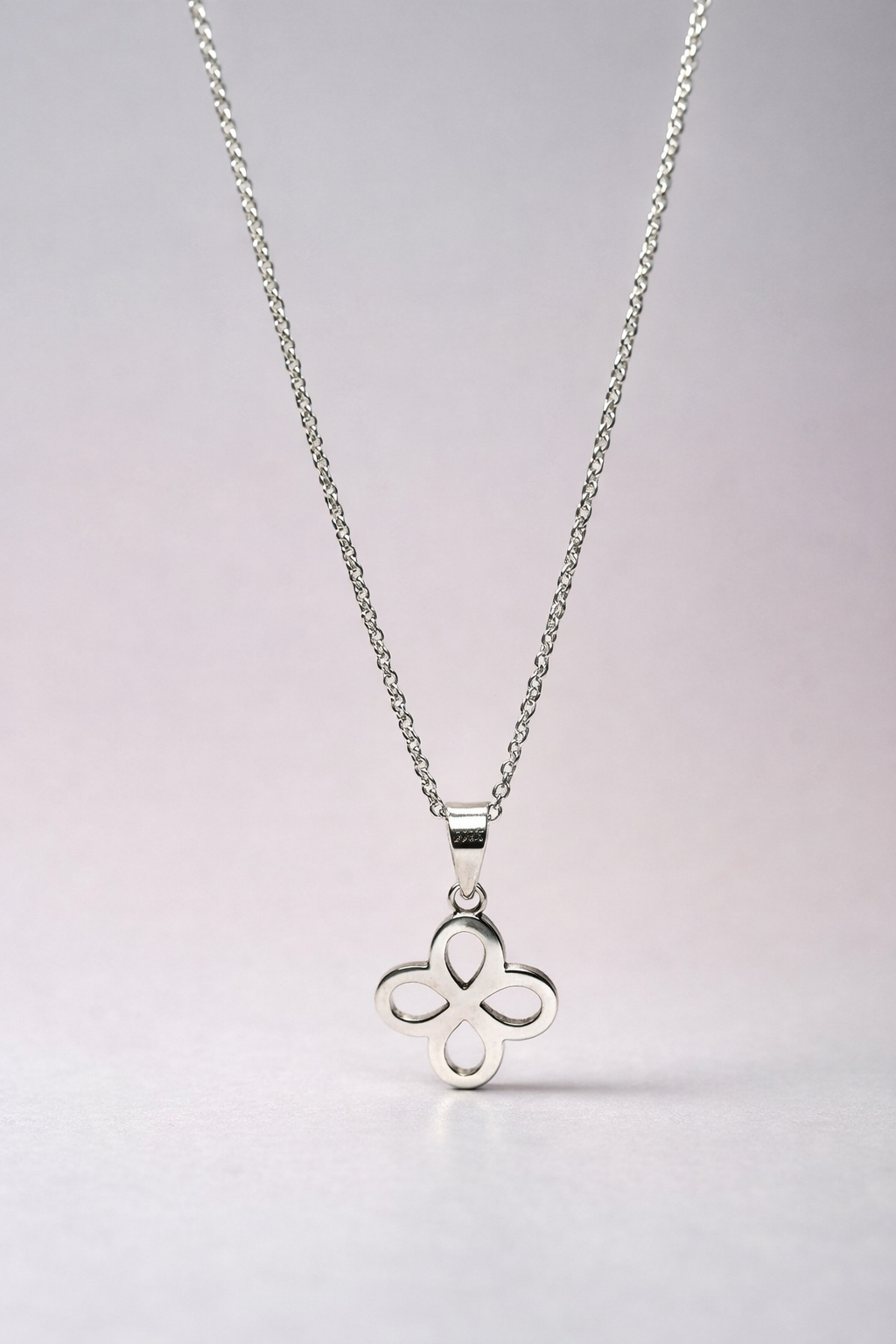 Silver necklace with a clover-shaped pendant on a light gray background