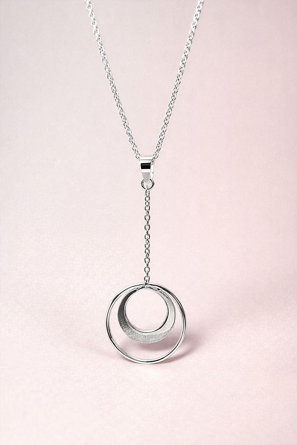 Silver necklace with a crescent circle pendant on a light pink background