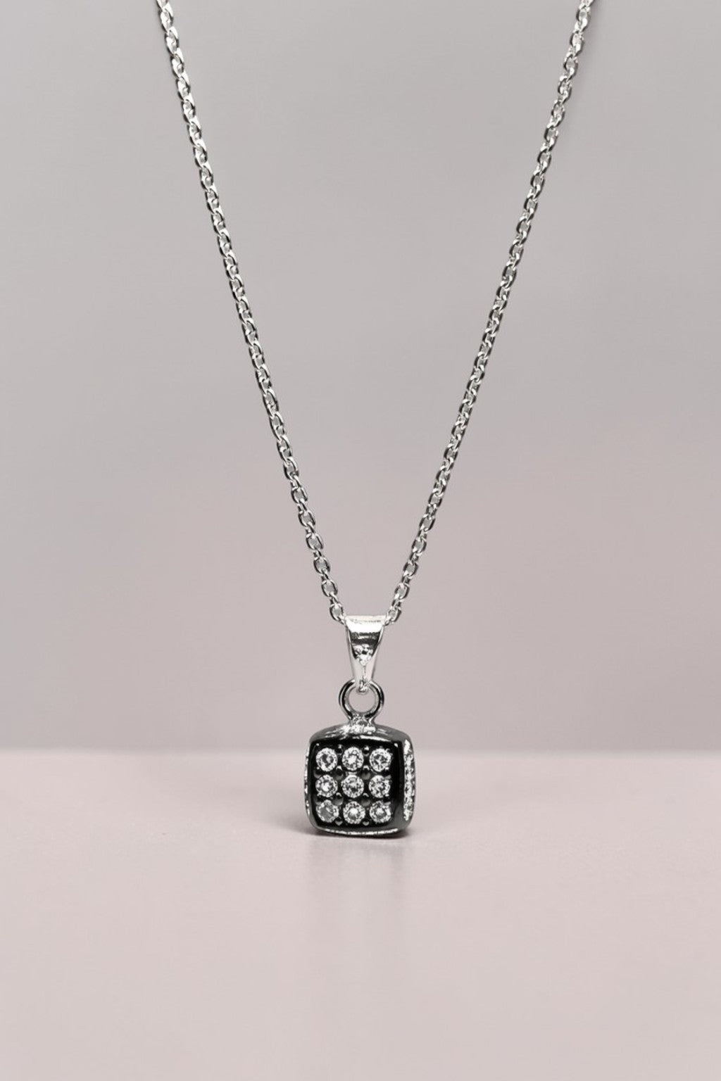 Silver necklace with a dice pendant on a gray background
