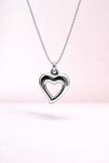 Heart-shaped silver pendant on a chain against a soft pink background