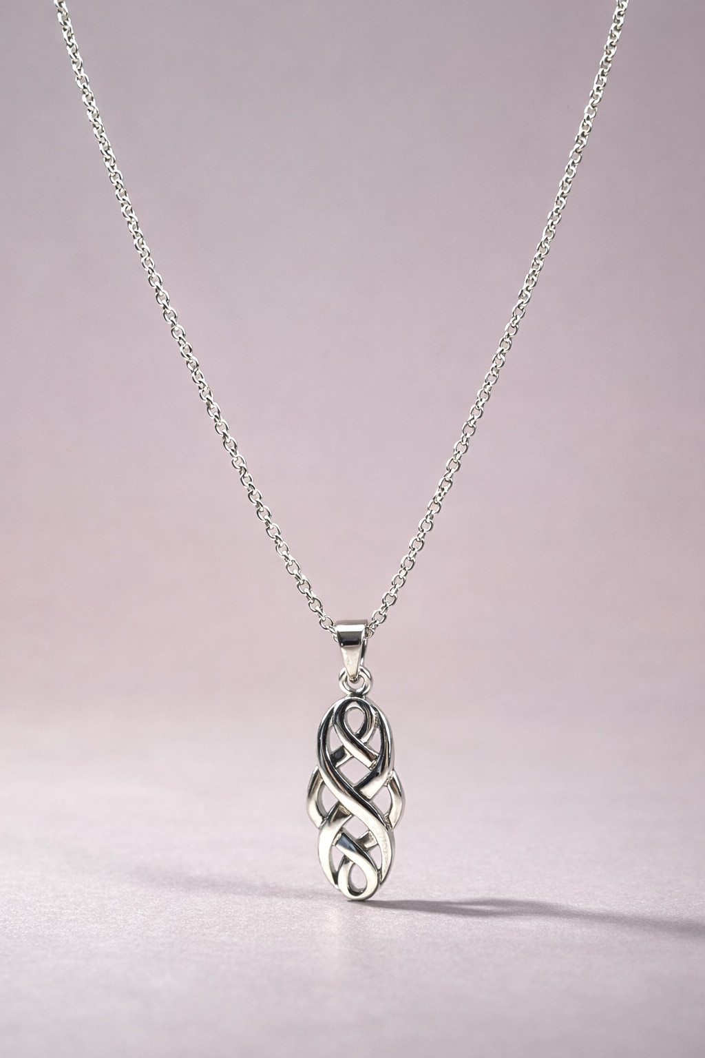 Silver necklace with a Celtic knot pendant on a light pink background