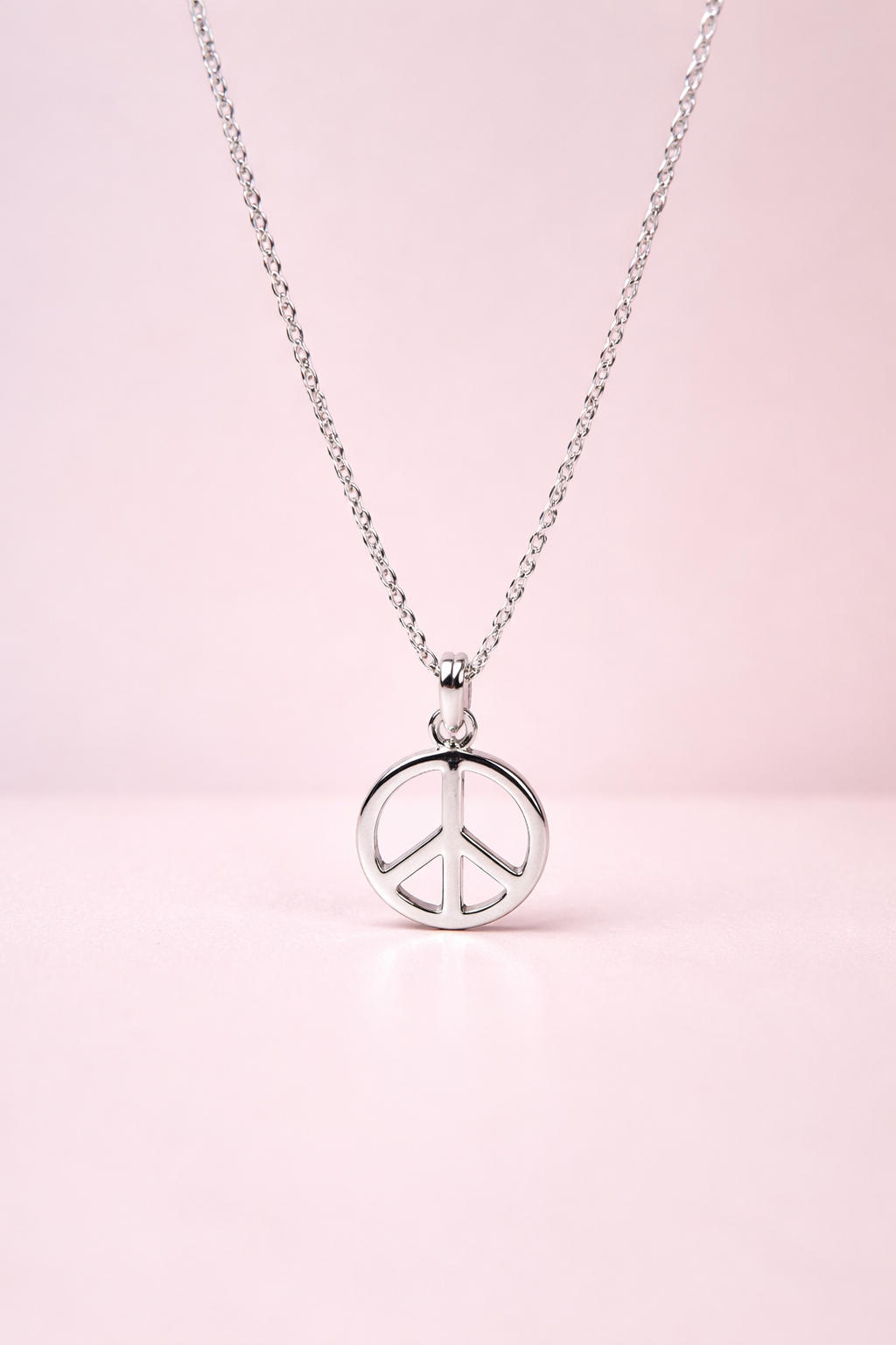 Silver peace sign necklace on a pink background