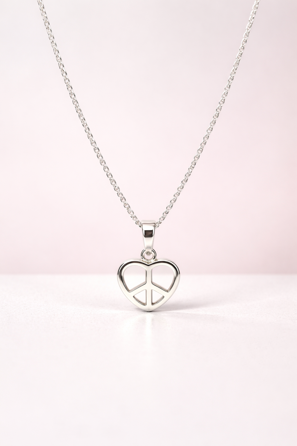 Silver necklace with a heart-shaped peace pendant on a light pink background