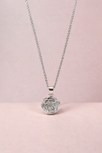 Silver necklace with a rose-shaped pendant on a pink background