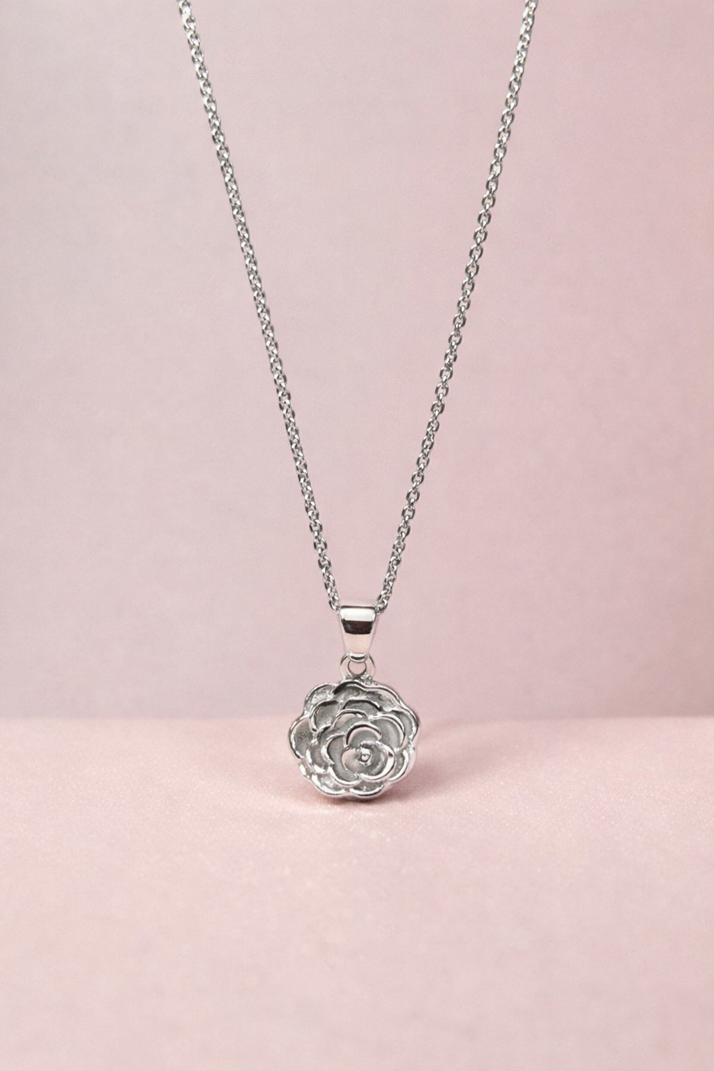 Silver necklace with a rose-shaped pendant on a pink background