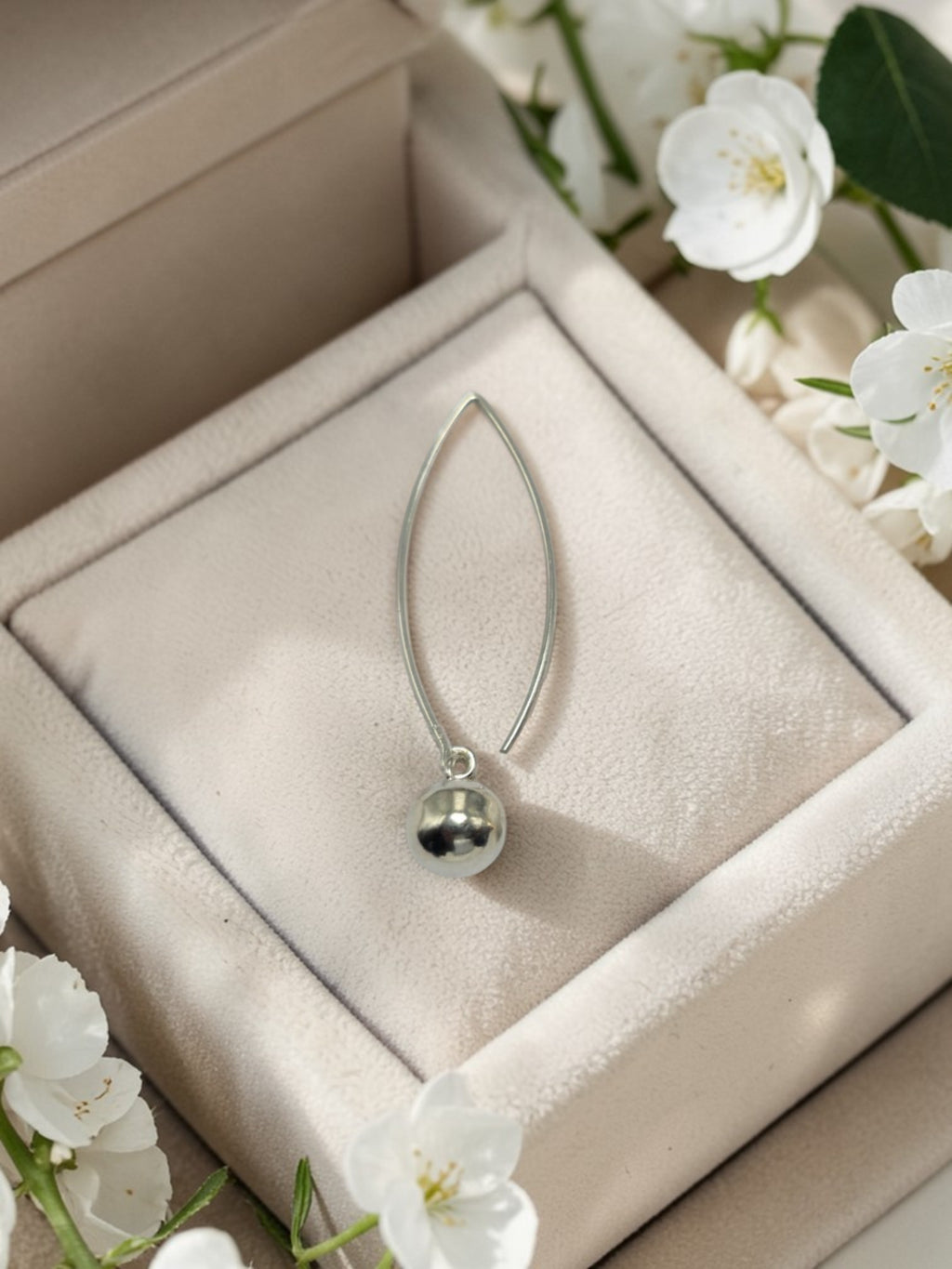 Silver teardrop-shaped pendant in a jewelry box with white flowers around