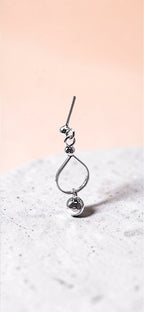 Silver teardrop-shaped pendant with a small round charm on a textured surface with a pink gradient background.